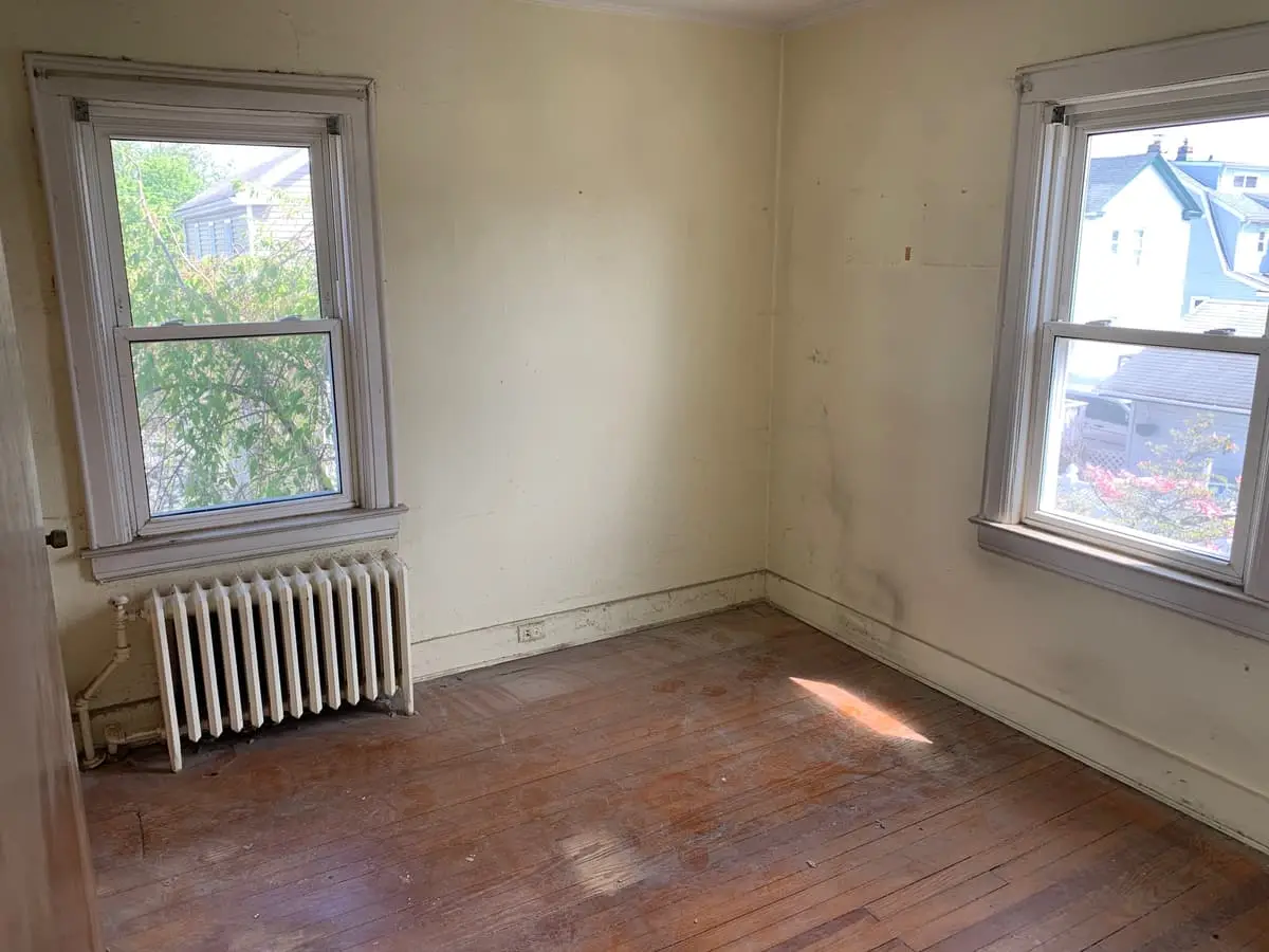 Selling a house as-is in Valley Stream: empty bedroom with stained floors and an old radiator